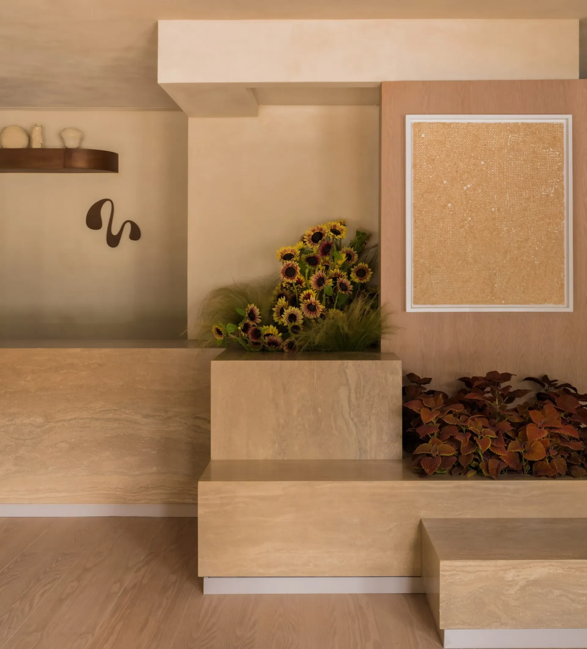 Travertine benches and planters with sunflowers beside a framed gold textured artwork on a pink plaster wall