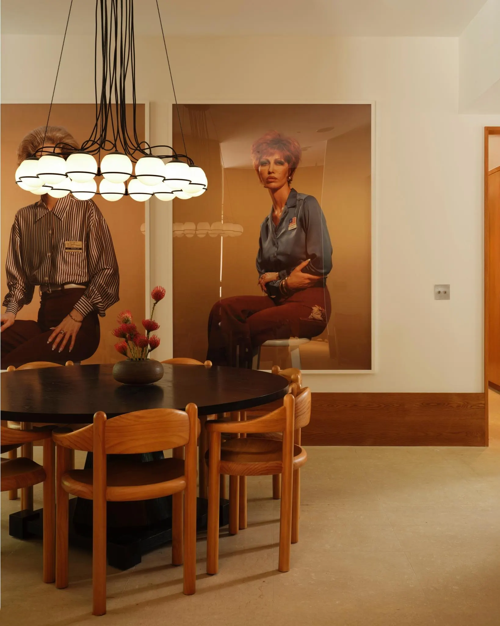Dining room with a round black table, globe chandelier and two large photographic portraits of seated figures