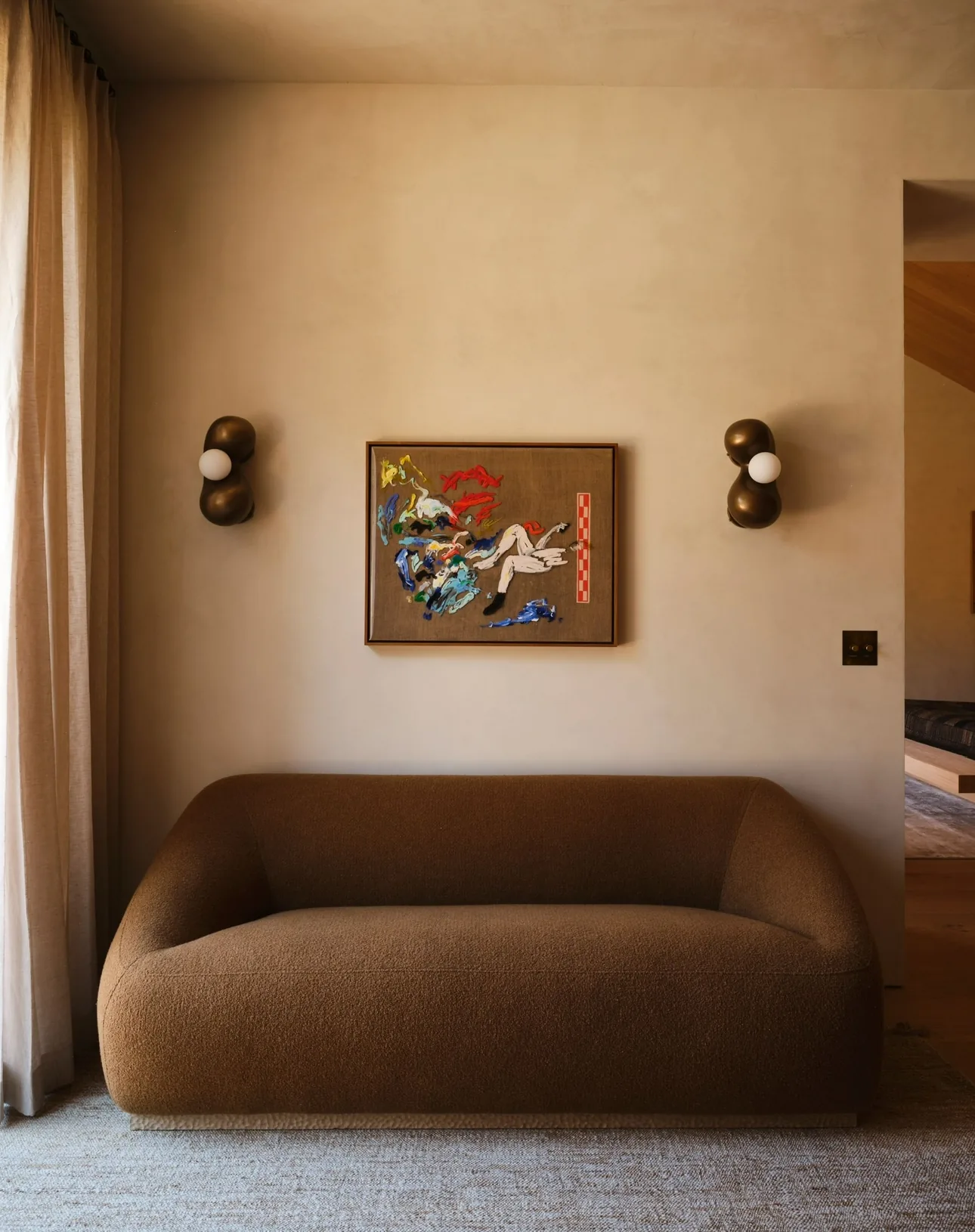 Small colorful figurative painting between bronze sconces above a curved boucle loveseat in a Chicago family home