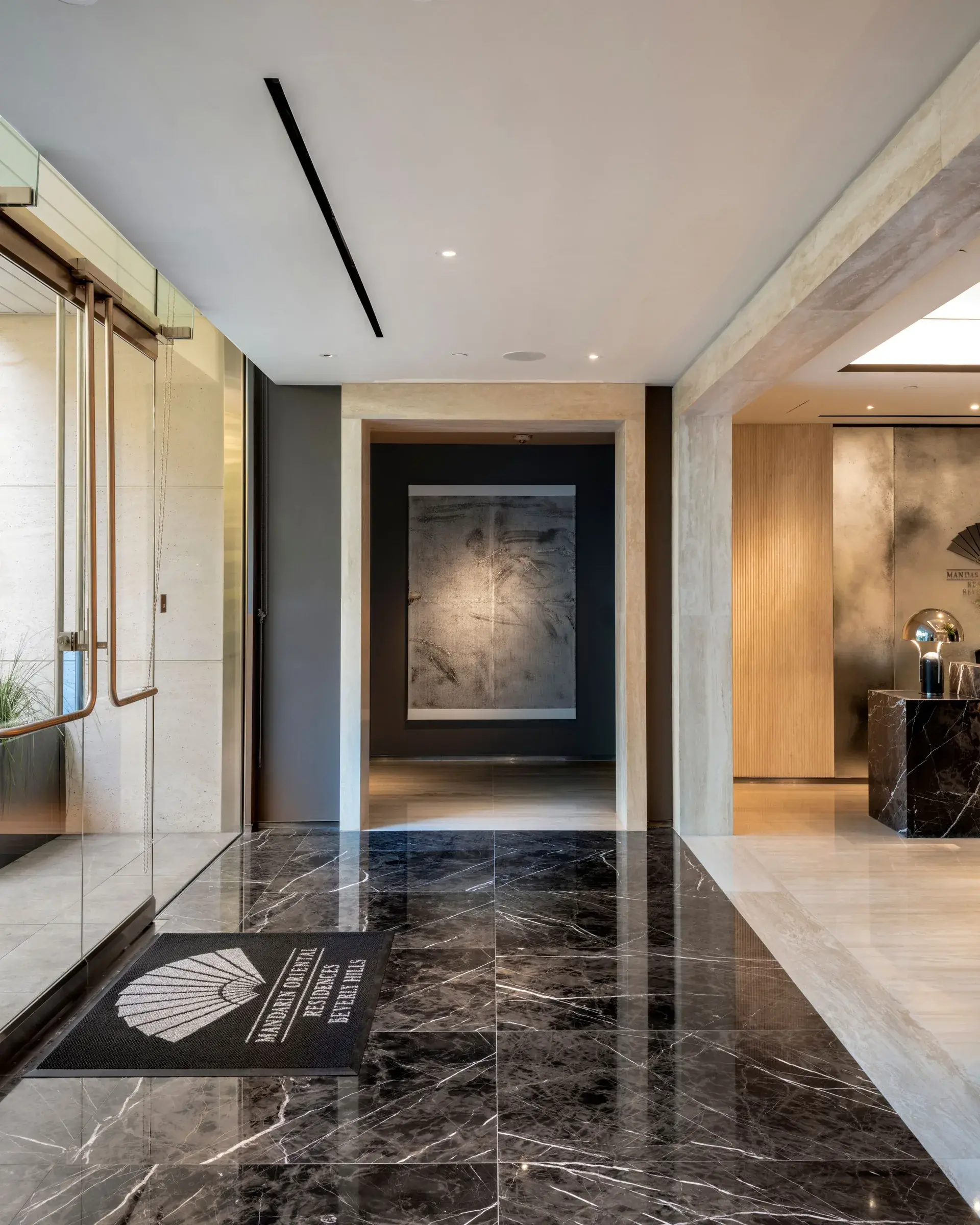 Residential lobby with dark marble floors and a large gray abstract artwork at the end of a corridor