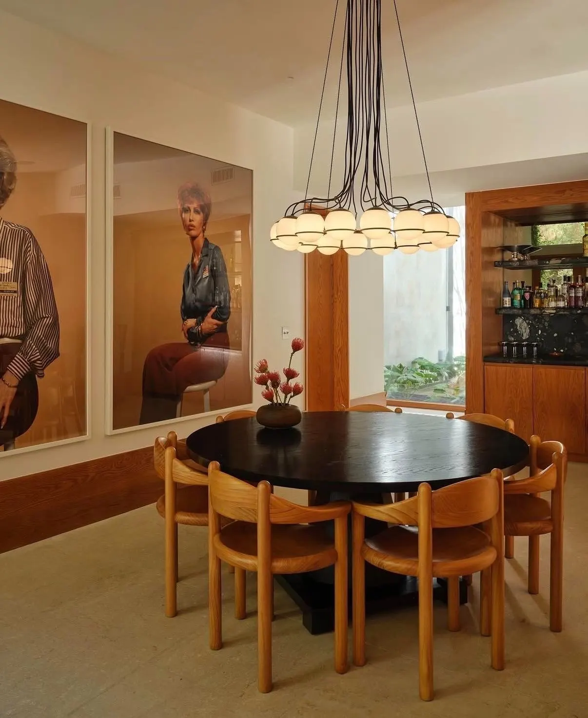 Dining room with two large photographic portraits of women beside a round black table and a globe chandelier