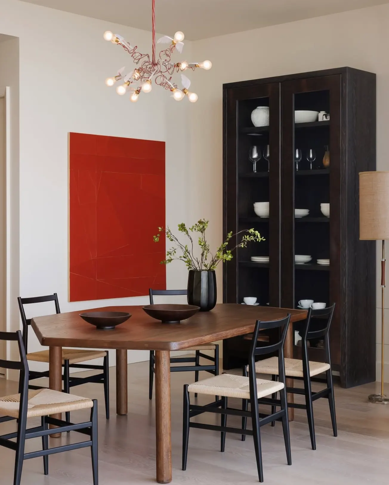 Large red abstract painting beside a dark glass-front cabinet in a dining room with a wooden table and rush chairs