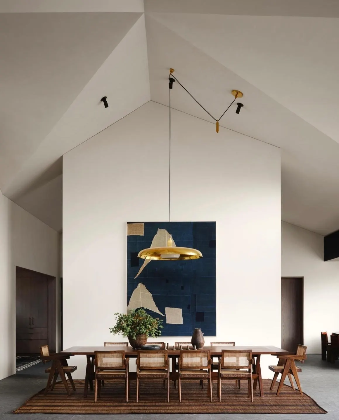 Vaulted white dining room with a large indigo patchwork textile artwork behind a long table and cane chairs