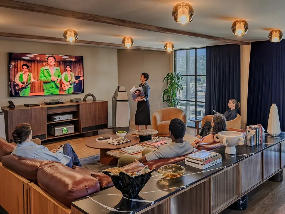 Office lounge with leather sofas, a wood media console and people gathered around a large screen
