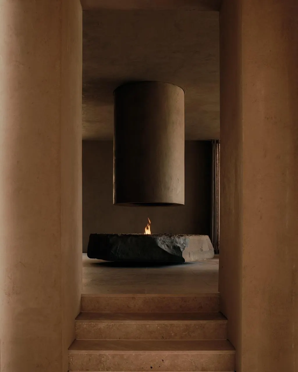 Stone fire pit beneath a suspended cylindrical plaster hood, seen through a narrow passage with stone steps